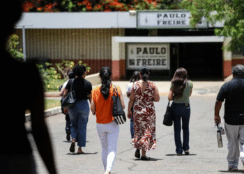 Pessoas vistas por trás caminhando em direção à entrada da Escola Paulo Freire em dia ensolarado