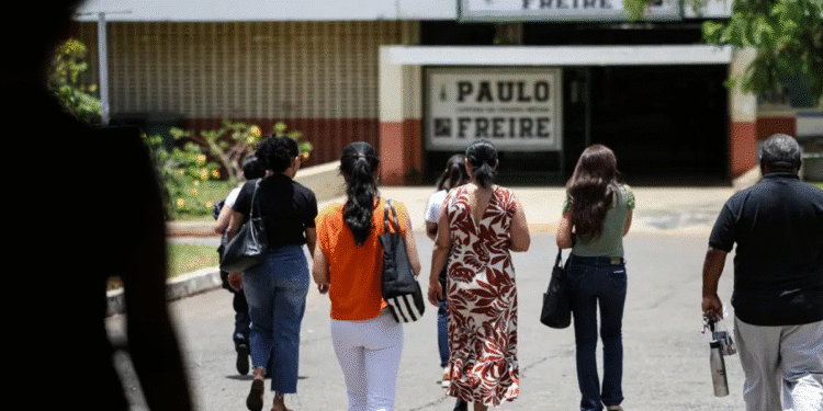 Pessoas vistas por trás caminhando em direção à entrada da Escola Paulo Freire em dia ensolarado