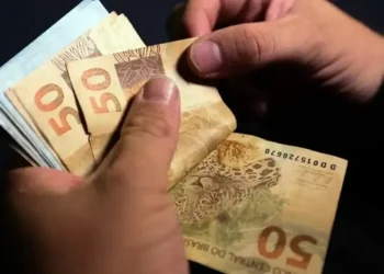 Mãos segurando notas de cinquenta reais representando bônus e pagamentos do Pé de Meia