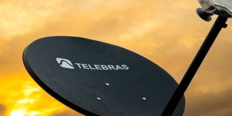 Antena parabólica preta da Telebras captando sinal durante o pôr do sol com céu laranja ao fundo