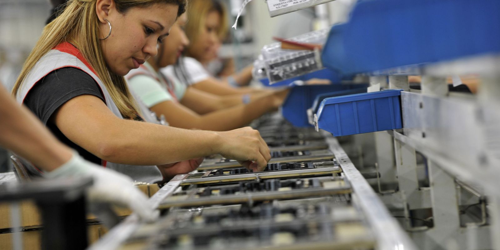 Linha de montagem industrial com trabalhadores focados Mulheres trabalhando em linha de montagem com uniformes e equipamentos de segurança em fábrica industrial