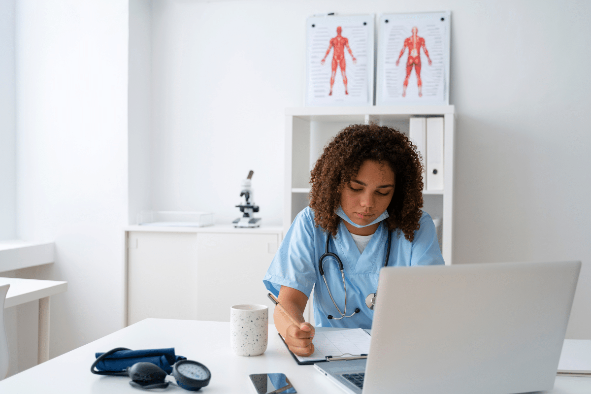 Enfermeira usando uniforme azul e estetoscópio, anotando em prancheta enquanto está em escritório clínico moderno