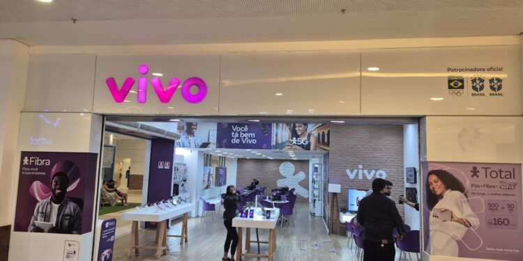 Fachada da loja Vivo em shopping com letreiro roxo, banners de fibra ótica e planos móveis, clientes dentro da loja