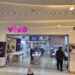 Fachada da loja Vivo em shopping com letreiro roxo, banners de fibra ótica e planos móveis, clientes dentro da loja