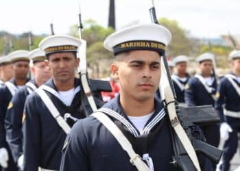 Soldados da Marinha do Brasil em uniforme azul-marinho e chapéu branco marchando em formação com rifles.