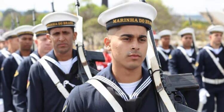 Soldados da Marinha do Brasil em uniforme azul-marinho e chapéu branco marchando em formação com rifles.
