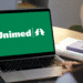 Computador com logo verde da Unimed na tela sendo usado por uma pessoa