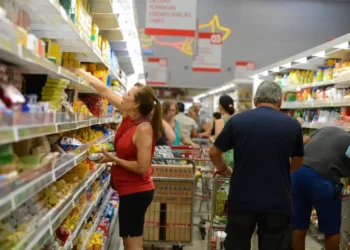 Supermercado cheio com consumidores comprando alimentos, ilustrando o impacto das novas regras do vale-refeição e vale-alimentação.