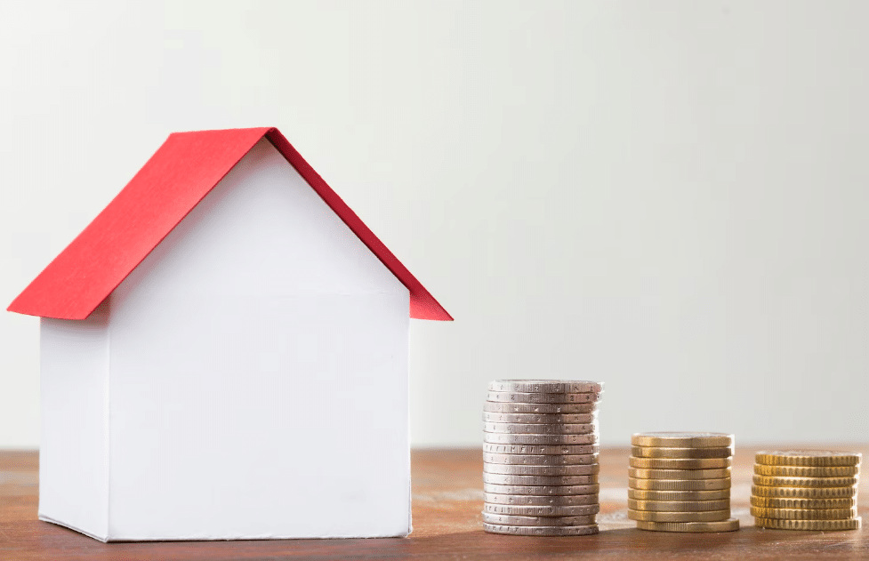 Modelo de casa ao lado de pilhas de moedas, representando faixas de renda e taxas de juros para reformas habitacionais.