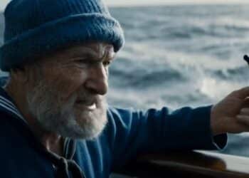 Homem idoso com boné azul e cachimbo, ao fundo do mar, evidenciando o semblante concentrado e intenso.
