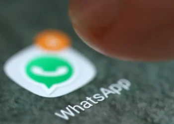 Foto da tela do celular mostrando o ícone do WhatsApp com uma notificação laranja e dedo próximo ao ícone