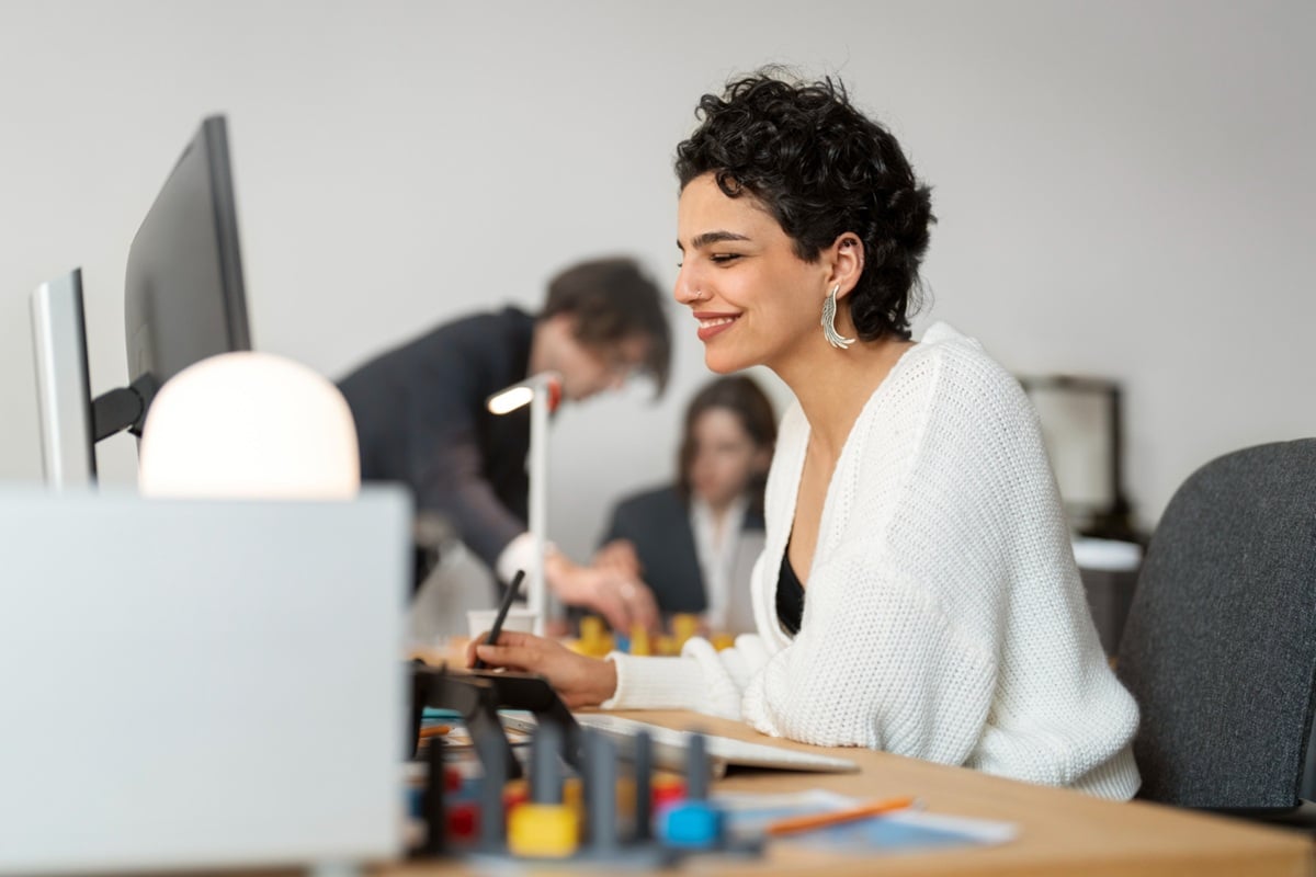 Profissional sorridente trabalhando em ambiente de escritório moderno com equipe ao fundo.