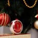 Relógio decorativo de Natal ao lado de bolas natalinas vermelhas e douradas em árvore de Natal.