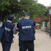 Dois agentes de pesquisa do IBGE usando coletes azuis identificados caminhando por rua durante trabalho de campo.