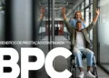 Homem em cadeira de rodas comemorando enquanto é empurrado por mulher em corredor corporativo, com destaque para o Benefício de Prestação Continuada (BPC).