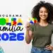 Mulher jovem de cabelos cacheados sorrindo e segurando o cartão do Bolsa Família 2026 com notas de 50 e 100 reais ao fundo.