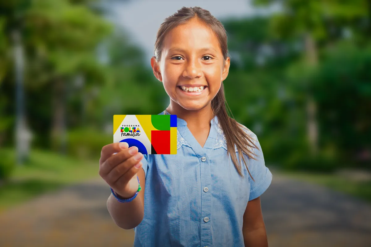 Bolsa Família Menina sorridente segurando cartão colorido do Programa Bolsa Família com fundo desfocado
