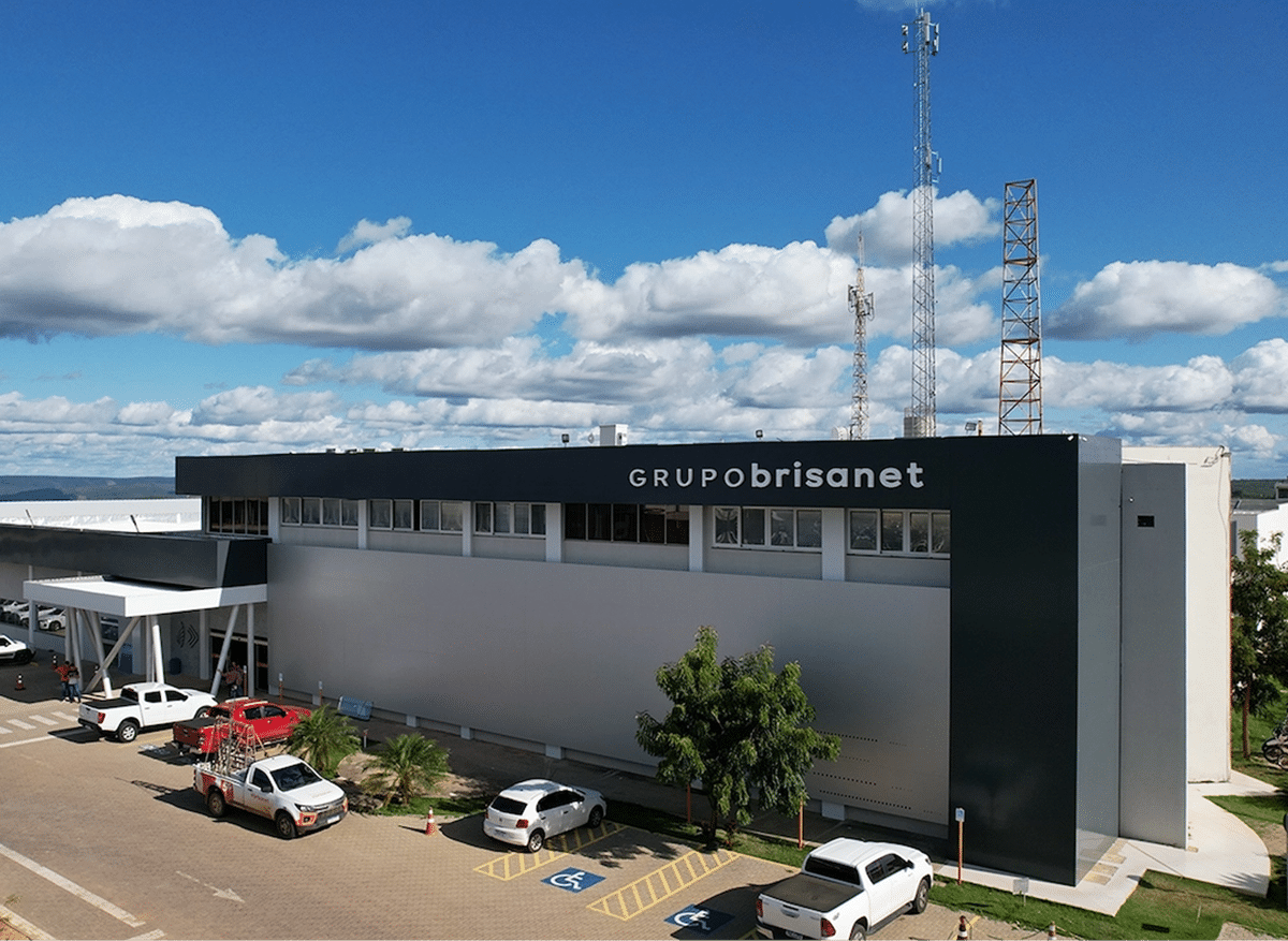 Fachada da sede do Grupo Brisanet com torres de telecomunicação e estacionamento.