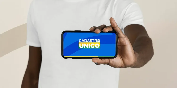 Pessoa exibindo um smartphone com a tela mostrando o logo do CadÚnico, indicando atualização para o ano de 2026.