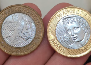 Duas moedas de 1 Real sendo seguradas entre os dedos: à esquerda, a edição de 25 anos com o Beija-Flor, e à direita, a edição de 30 anos com a efígie da República.