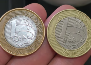 Close-up de diversas moedas de 1 real brilhantes agrupadas sobre uma superfície, destacando o desenho e o ano de fabricação.