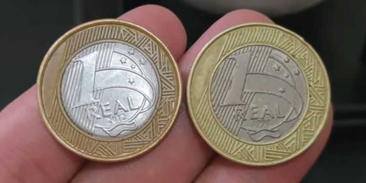 Close-up de diversas moedas de 1 real brilhantes agrupadas sobre uma superfície, destacando o desenho e o ano de fabricação.