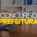 Tela com texto "CONCURSO PREFEITURA" sobre mesa com notebook e estante de livros ao fundo.