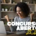 Mulher feliz comemorando diante do laptop com texto concursos abertos 2026 em destaque