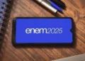 Logo do Enem 2025 exibido em um smartphone sobre uma mesa de estudos, representando o Exame Nacional do Ensino Médio.