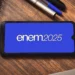 Logo do Enem 2025 exibido em um smartphone sobre uma mesa de estudos, representando o Exame Nacional do Ensino Médio.