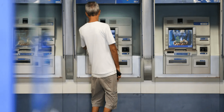 Homem de camiseta branca usando caixa eletrônico da Caixa com opção de saques e depósitos.