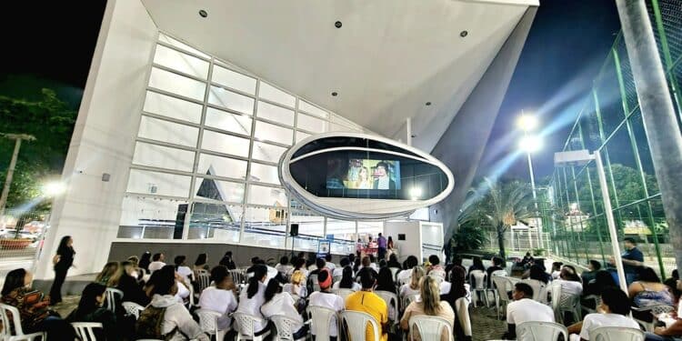 Fachada iluminada da Nave do Conhecimento durante evento noturno com público ao ar livre.