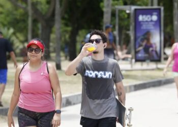 Pessoas andando ao ar livre sob altas temperaturas, demonstrando a importância da hidratação e da proteção contra o calor no verão