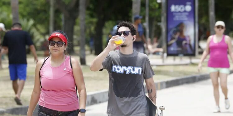 Pessoas andando ao ar livre sob altas temperaturas, demonstrando a importância da hidratação e da proteção contra o calor no verão
