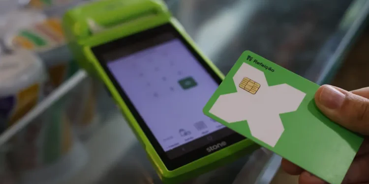 Mão segurando cartão de refeição verde próximo a maquininha Stone para pagamento