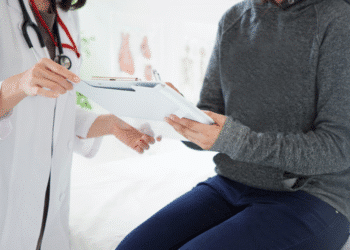 Médico entregando documento para paciente sentado durante avaliação médica.