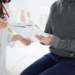 Médico entregando documento para paciente sentado durante avaliação médica.