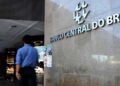 Fachada do Banco Central do Brasil com homem de camisa azul caminhando em frente ao prédio
