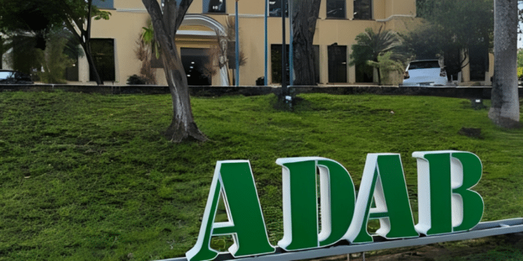 Letreiro verde com as letras ADAB na fachada de prédio institucional cercado por árvores e área verde