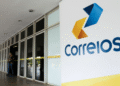 Entrada da agência dos Correios com logo colorida em destaque na parede branca.
