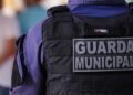 Detalhe do colete tático preto com placa "Guarda Municipal" na parte de trás do uniforme azul
