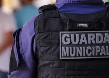 Detalhe do colete tático preto com placa "Guarda Municipal" na parte de trás do uniforme azul