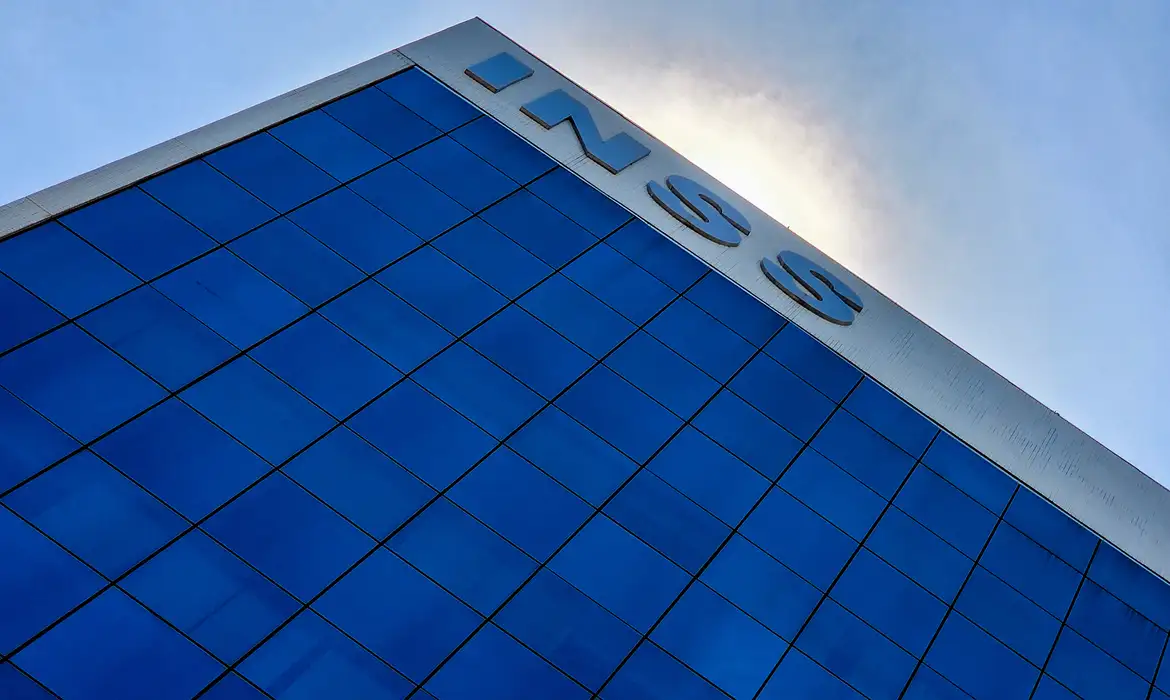 Fachada de prédio corporativo com janelas azuis e logo do INSS no topo em metal prateado