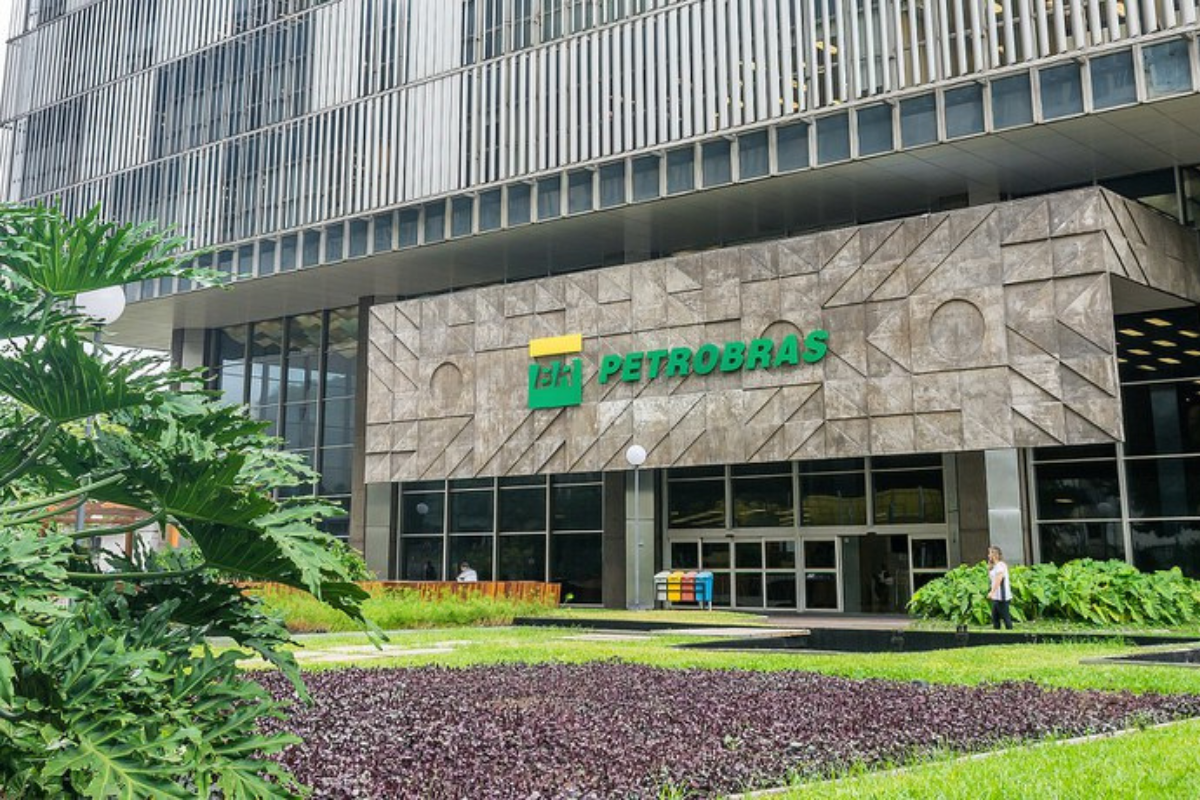 Concurso Petrobras 2026 Fachada da sede da Petrobras com área verde, plantas e pessoas em frente ao prédio moderno.