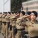 Policiais militares femininas alinhadas em formação realizando saudação com uniforme bege e boina preta