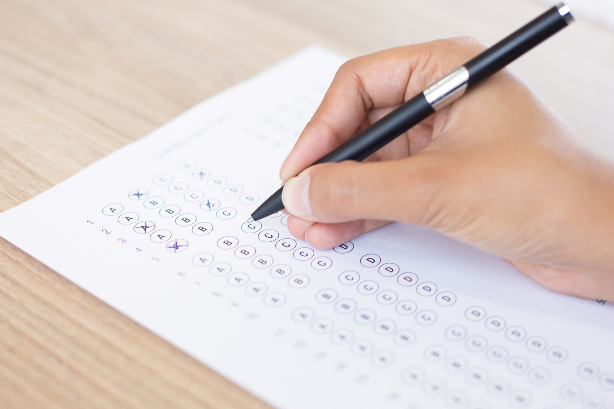 Mão preenchendo resposta de teste de múltipla escolha em papel com caneta preta