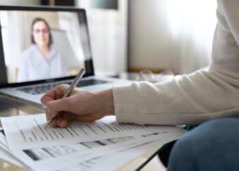 Pessoa preenchendo documentos durante entrevista por vídeo em laptop