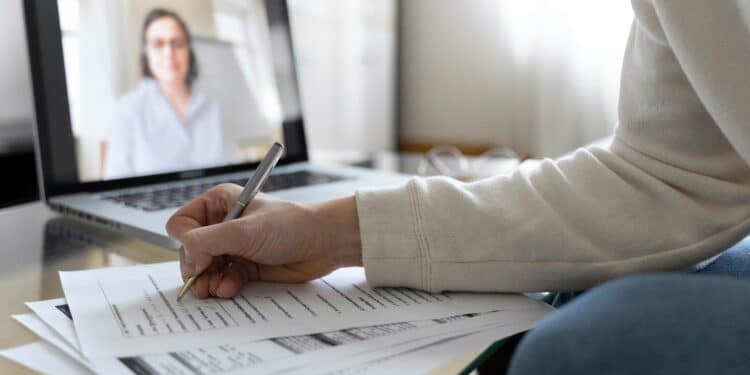 Pessoa preenchendo documentos durante entrevista por vídeo em laptop