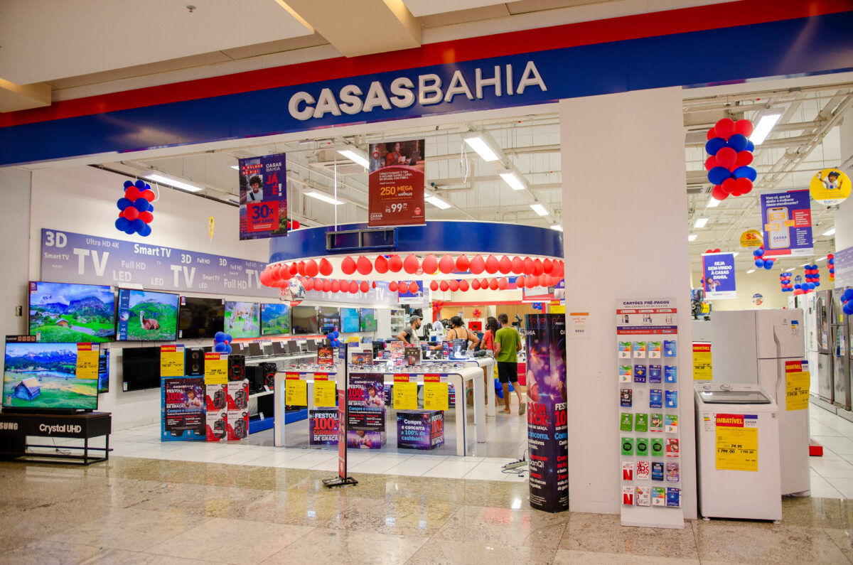 Fachada da loja Casas Bahia com decoração de balões vermelhos e azuis, oferecendo TVs, geladeiras e produtos eletrônicos.
