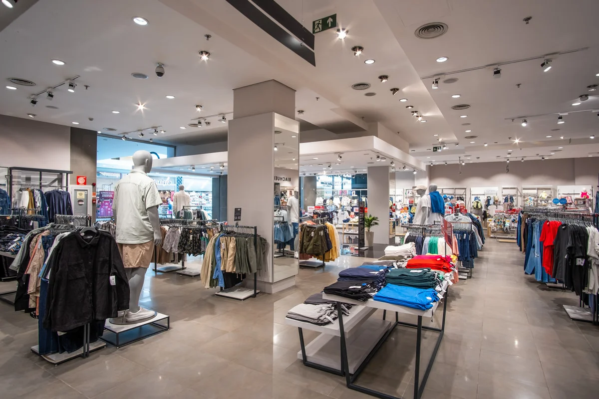 Emprego Riachuelo Interior de loja de roupas com manequins, cabides e mesas organizadas com roupas coloridas e ambiente amplo.